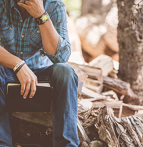 Tischlerei H&B Design in Langenberg | Ansprechpartner Ein denkender Mann mit einem Buch neben mehreren Holzscheiten
